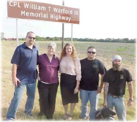 Liz Kennedy | The Rosebud News            Sgt. James Hallam, Jere Beal, Crystal Bethke, Sic ret. Thomas Crockett, and Dean Ross with his dog Warford under the new sign dedicating the road to Cpl. William Warford III.